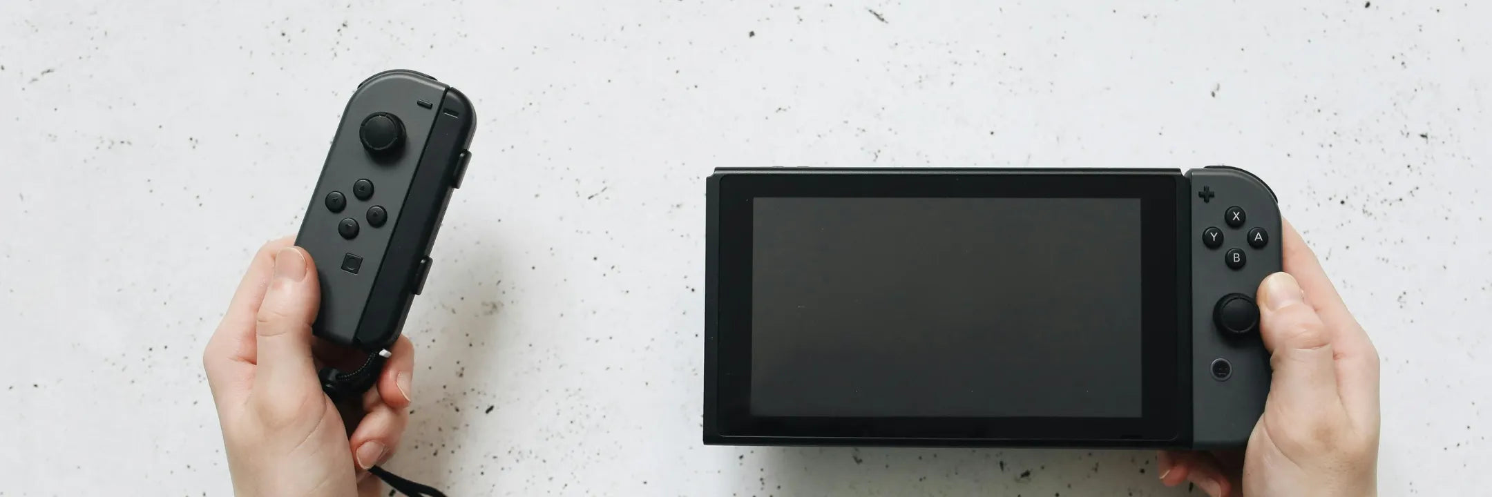 Person holding a Nintendo Switch controller with the console on a white surface, ideal for gaming enthusiasts.