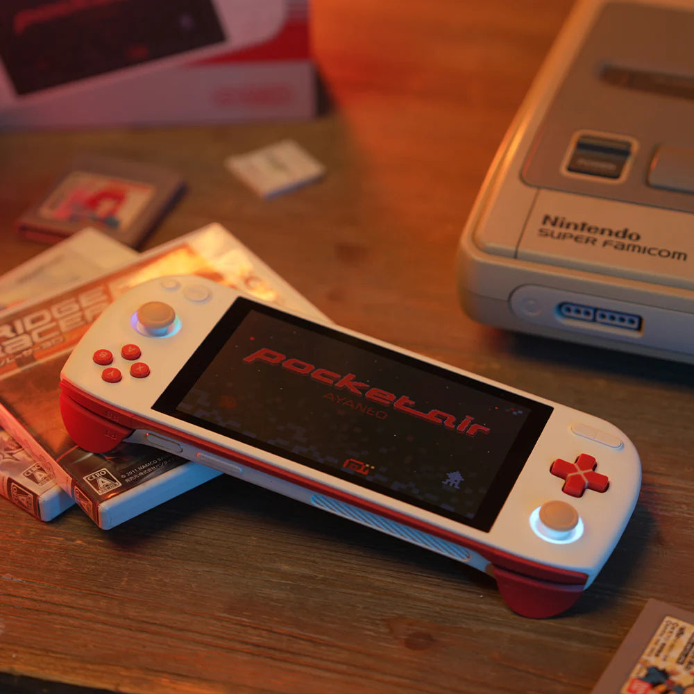 Console AYANEO Pocket AIR affichant un jeu, avec des cartouches et un ancien jeu vidéo en arrière-plan.
