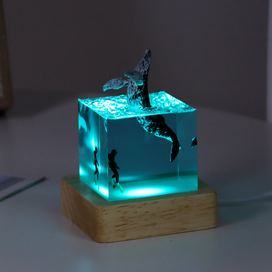 Veilleuse cube en résine, queue de baleine émergeant du cube, sur socle lumineux en bois