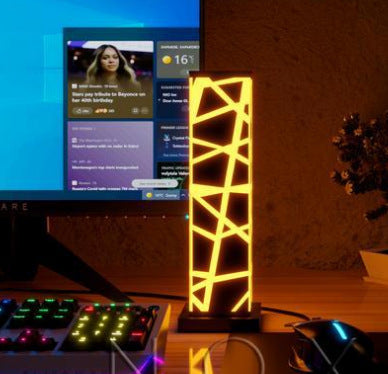 Lampe colonne en acrylique, motif treillis lumineux allumé en jaune, sur un bureau